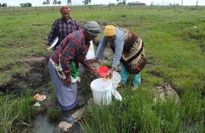Mancam villagers use a small strainer to catch fungi, worms and other debris found in the murky spring water they rely on. | Photo: Mkhuseli Sizani